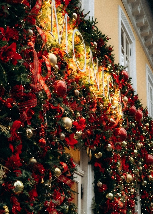 Christmas window decorated with red baubles, fir garland, and warm fairy lights on a golden facade