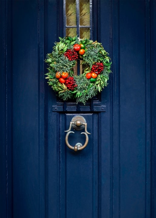 Round Christmas wreath with berries and citrus hanging on a navy blue front door