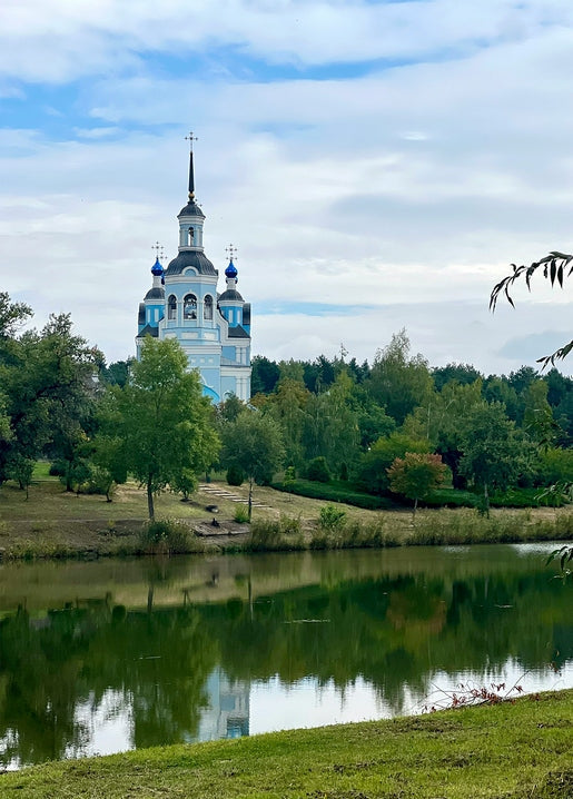A blue-domed church and its reflection in a calm lake, surrounded by trees in the Poltava region.