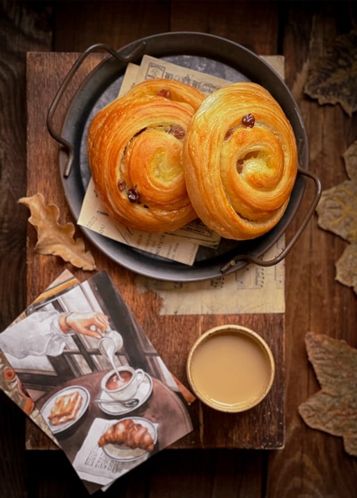 Zimtschnecken mit Rosinen und Milchkaffee auf einem herbstlichen Holztablett
