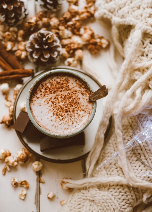 Mug of hot cocoa with cinnamon, pinecones and a cream knit blanket
