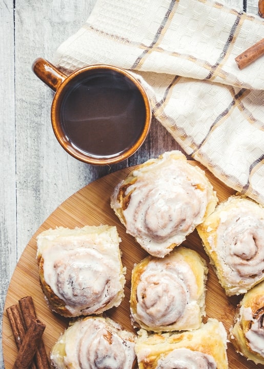 Glasierte Zimtschnecken mit einer Tasse Kaffee und Zimtstangen