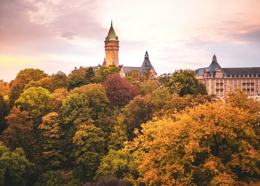 Steinturm mit grüner Spitze über Kuppeldächern und goldenen Herbstbaumkronen bei Sonnenuntergang