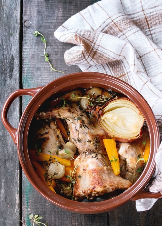 Tontopf mit geschmortem Hähnchen, Karotten, Knoblauch und Thymian auf einem Holztisch