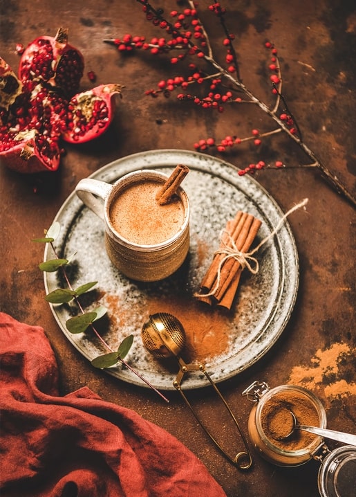 Mug of cinnamon-dusted cocoa with pomegranate, red berries, and eucalyptus on a rustic table