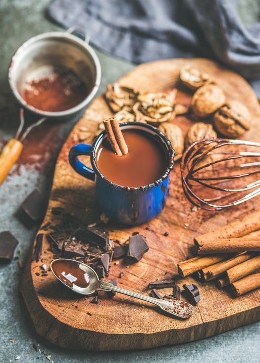 Blue enamel mug of hot chocolate with cinnamon, walnuts, and chocolate chunks on wood