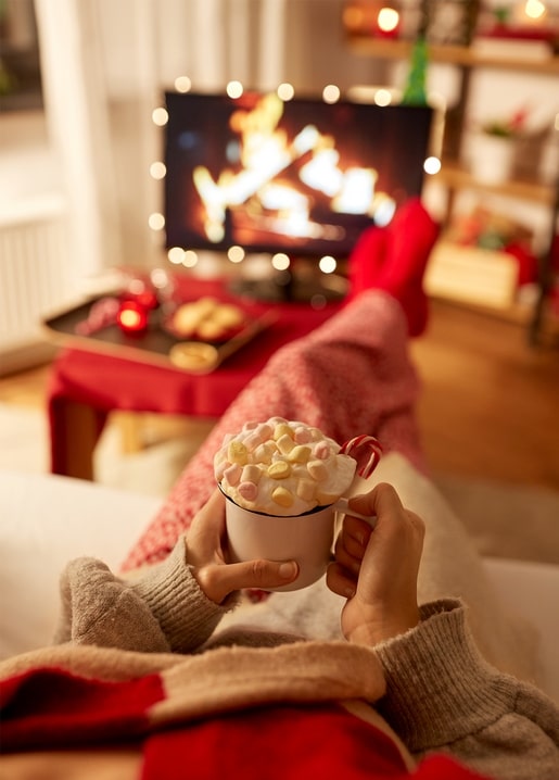 Feet in red socks holding a cocoa mug with marshmallows in front of a TV fireplace video