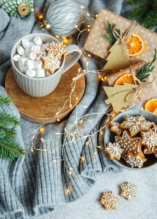Mug of cocoa with a gingerbread snowflake beside wrapped gifts and fairy lights