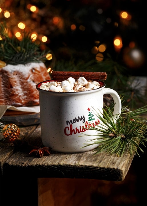 Mug of hot cocoa with marshmallows and a cinnamon stick beside a gingerbread cake