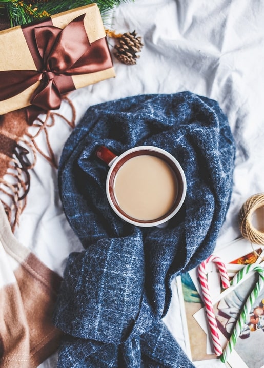 Mug of cocoa in a blue plaid scarf beside a gift box and candy canes