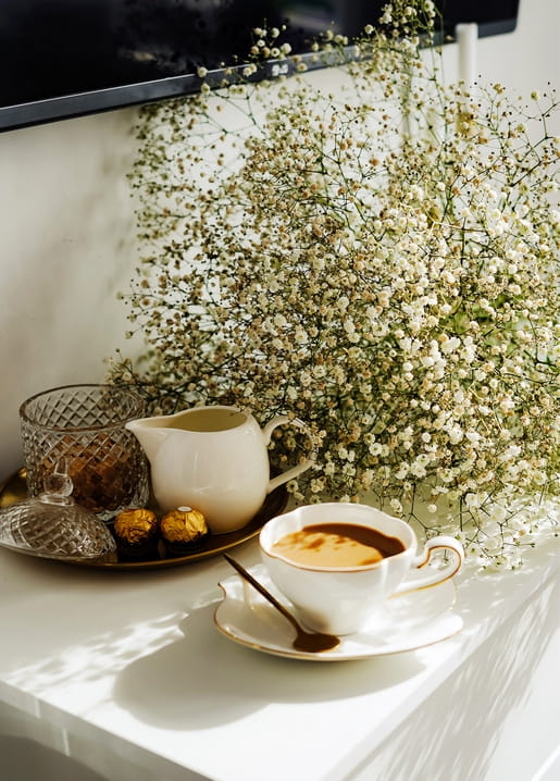 Kaffeetasse aus Porzellan mit Zuckerdose und Schleierkraut auf weißem Tisch