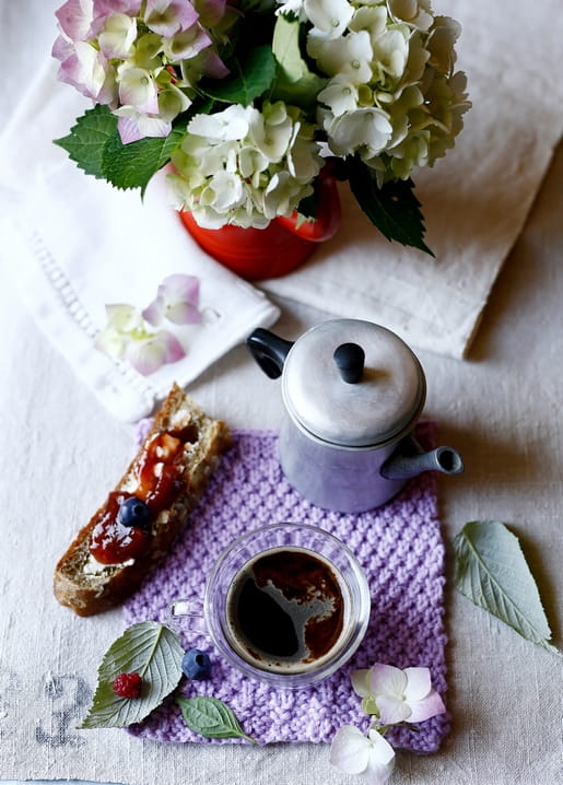 Red mug of hydrangeas, vintage coffee pot and toast with jam on a purple knitted cloth