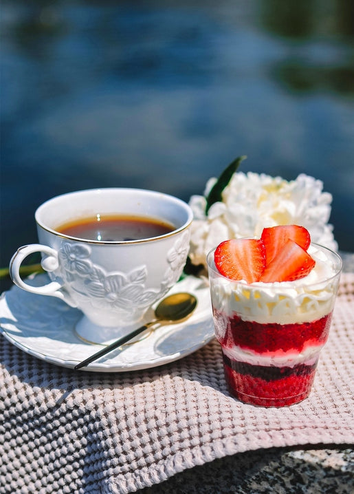 Coffee cup, strawberry parfait, and white peony on a table by the sea