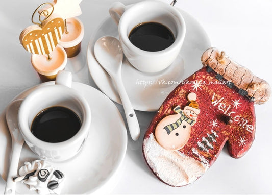 Zwei Kaffeetassen neben einem Lebkuchen-Fäustling mit 'Welcome'-Schneemann
