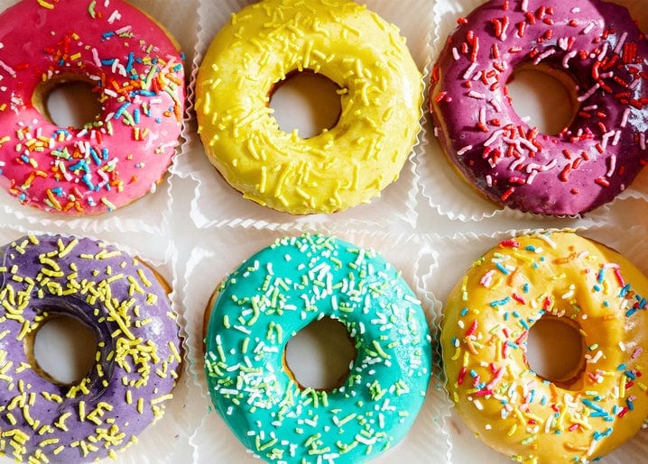 Six donuts with pink, yellow, magenta, purple, teal, and orange glaze and sprinkles