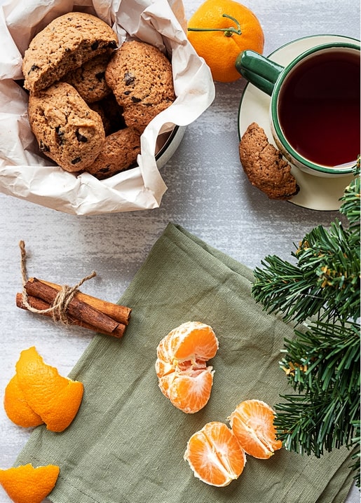 Oatmeal cookies, peeled tangerines and tea beside a pine branch