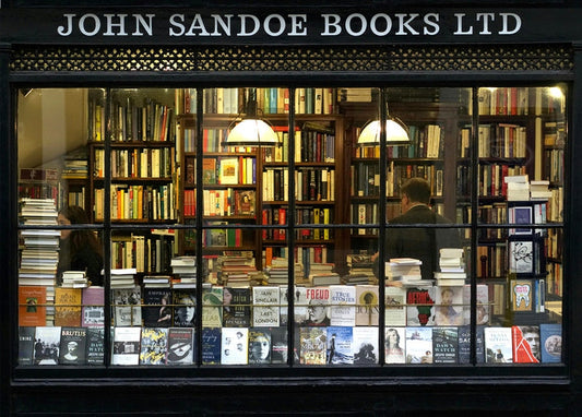 Bookshop window filled with stacked books under warm lamp light
