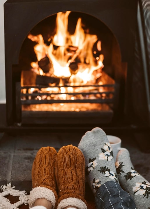 Two pairs of feet in cozy knit socks warming by a crackling fireplace