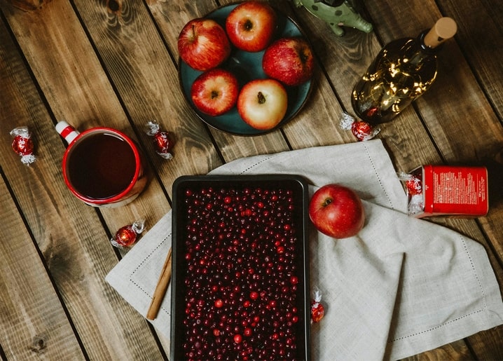 Flat lay of cranberries, apples, tea, and wrapped sweets on a wooden table
