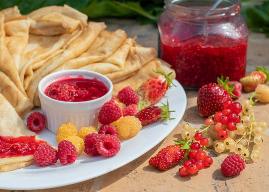 Folded crepes with berry jam, raspberries, strawberries and currants on a plate