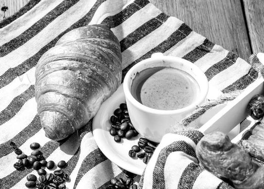 Black-and-white photo of a croissant, espresso cup, and coffee beans on striped cloth