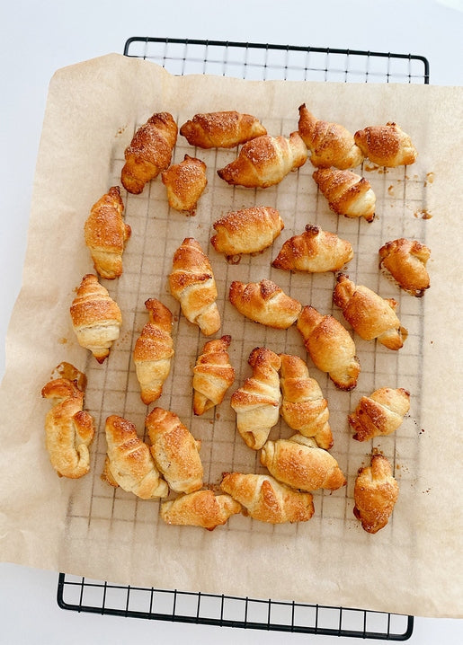 Golden croissants dusted with sugar cooling in rows on a wire baking rack