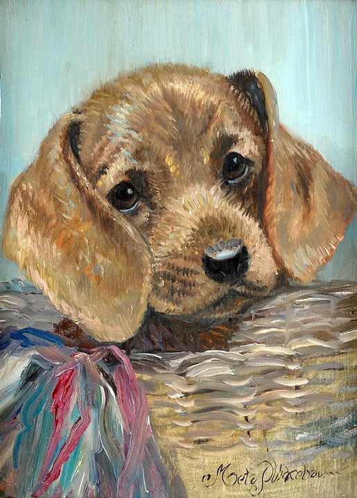 Tan dachshund puppy with floppy ears peeking out of a woven basket beside a colorful fringed cloth
