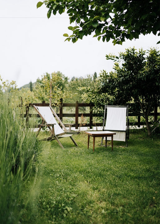Two empty folding deck chairs on a garden lawn beside a wooden fence and small table