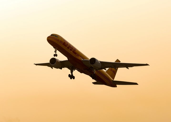 DHL-Frachtflugzeug im Start vor orangefarbenem Sonnenuntergangshimmel