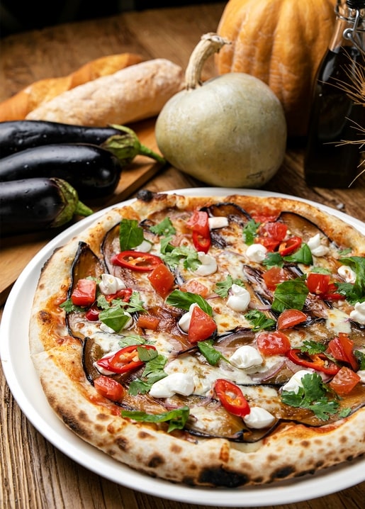 Auberginen-Tomaten-Pizza neben frischen Auberginen und Brot