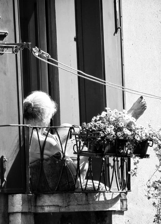 Schwarzweißfoto einer älteren Frau auf dem Balkon zwischen Blumentöpfen, Fuß auf der Wäscheleine