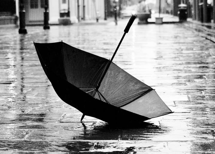 Ein umgestürzter Regenschirm liegt auf nassem Kopfsteinpflaster einer Regenstraße, Schwarzweißfoto