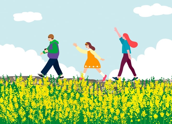 Family of three waving while walking through a yellow flower field with mountains behind