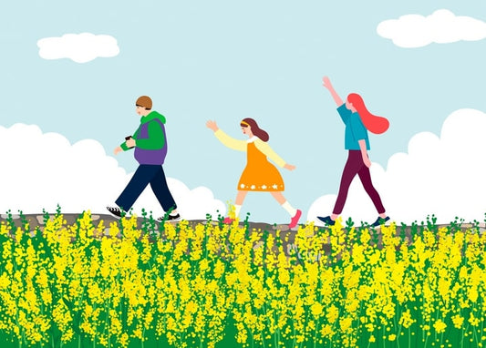 Family of three waving while walking through a yellow flower field with mountains behind