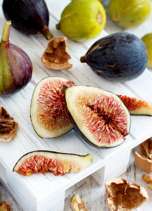 Halved purple and green figs with cracked walnuts arranged on a white wooden board