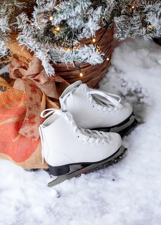 White figure skates beside a burlap-wrapped gift and a lit pine branch in snow