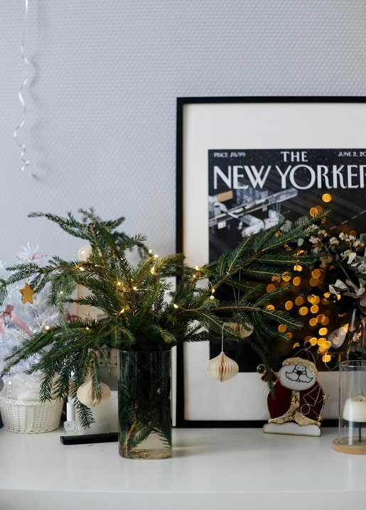 Fir branches with fairy lights and paper ornaments beside a framed magazine print