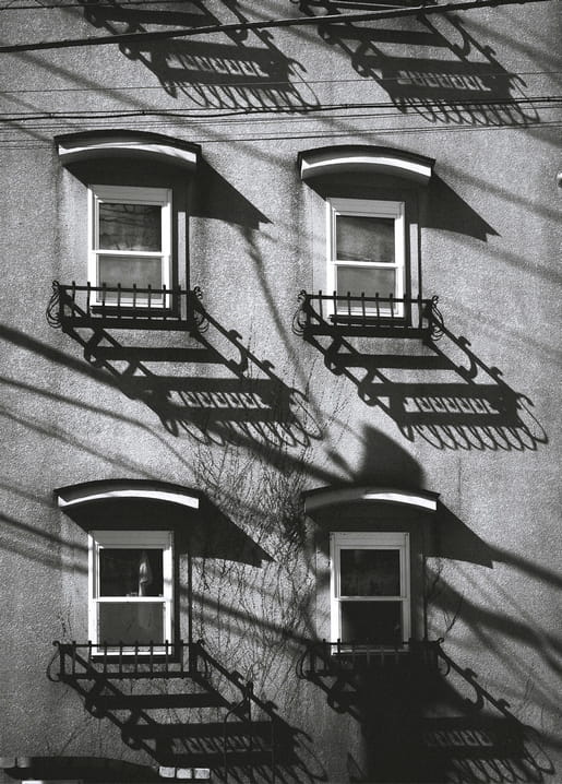 Hausfassade mit vier schmiedeeisernen Feuertreppen und langen diagonalen Schatten