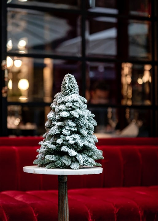 Small flocked Christmas tree on a marble café table with a red velvet banquette behind