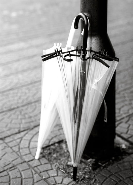 Translucent folded umbrella leaning against a lamppost on patterned cobblestones