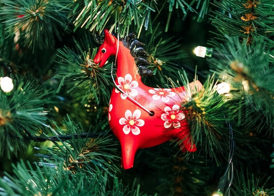 Red floral folk-horse ornament hanging on a lit Christmas tree