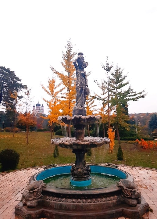 Sculpted fountain in Feofania Park with golden ginkgo trees and church domes in the distance