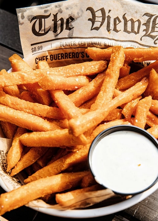 Korb knuspriger Pommes frites mit cremigem Dip auf einem Tablett mit Zeitungspapier