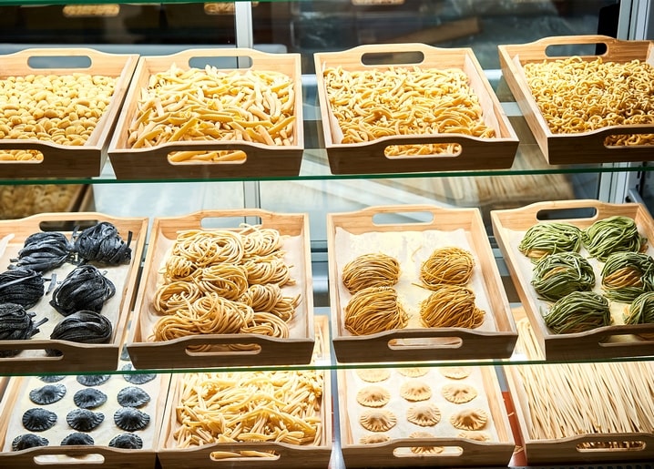 Holzkisten mit hausgemachter Pasta — Tagliatelle, Tintenfisch-Nudeln und Ravioli — hinter Thekenglas