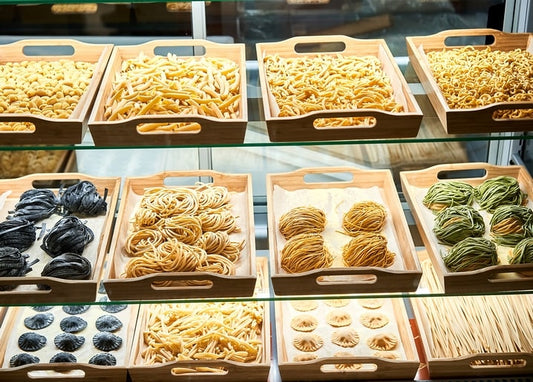 Holzkisten mit hausgemachter Pasta — Tagliatelle, Tintenfisch-Nudeln und Ravioli — hinter Thekenglas