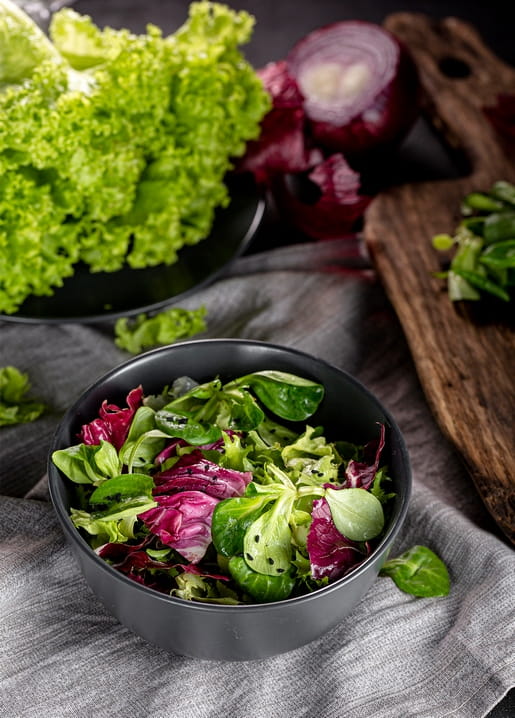 Bowl of fresh mixed salad with lettuce, radicchio and red onion on a wooden board