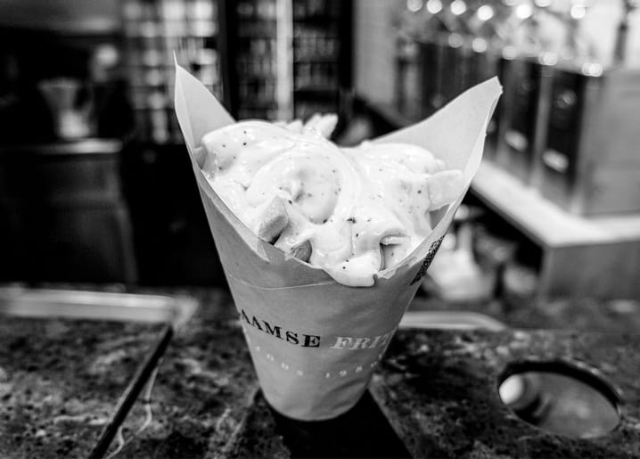 Papiertüte mit Pommes und Mayonnaise auf einer Bartheke, Schwarzweißfoto.