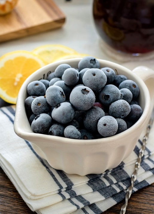 Schale mit gefrorenen Blaubeeren, Zitrone und einem Glas Eistee