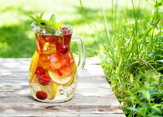 Glass pitcher of fruit-infused water with lemon, strawberries and cherries on a wooden table in summer grass