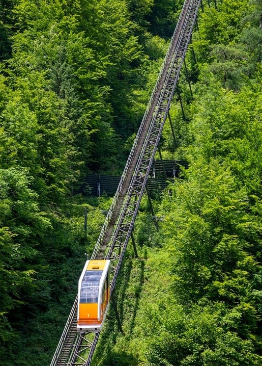 Orange funicular car climbing tracks through a dense green summer forest